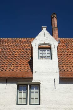 White brick house with three windows and red roof. (Bruges, Belgium). Blue sky in the background.