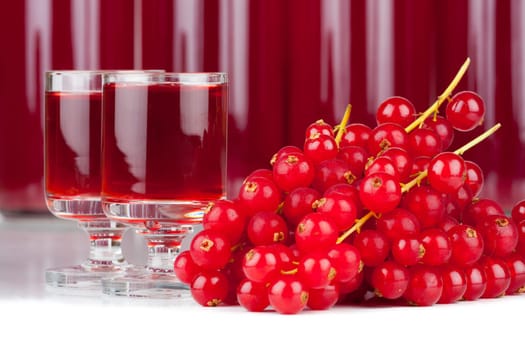 Close-up view of ripe red currants and syrup in a glass and bottles isolated on white background