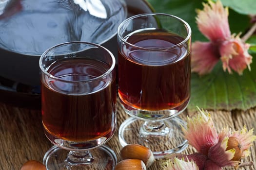 Homemade hazelnut liqueur in two glasses with hazelnuts on old wooden board
