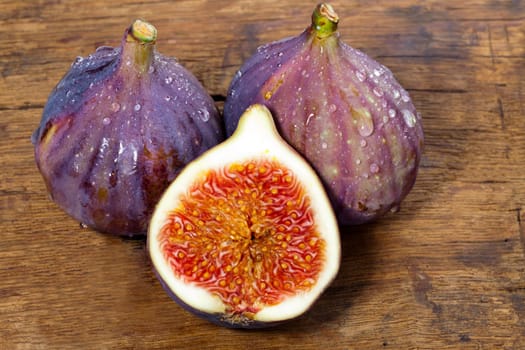 Two whole and one half fresh figs on old rustic wooden board