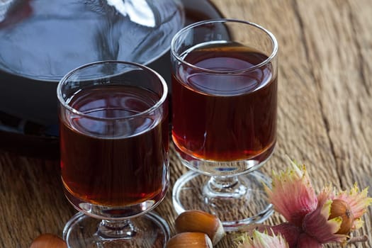 Close-up view of homemade hazelnut liqueur in a carafe and a glass with hazelnuts on wooden board
