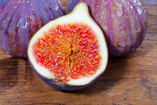 Two whole and one half fresh figs on old rustic wooden board