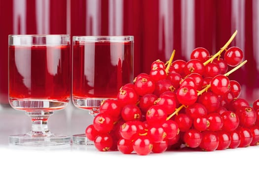 Close-up view of ripe red currants and syrup in a glass and bottles isolated on white background