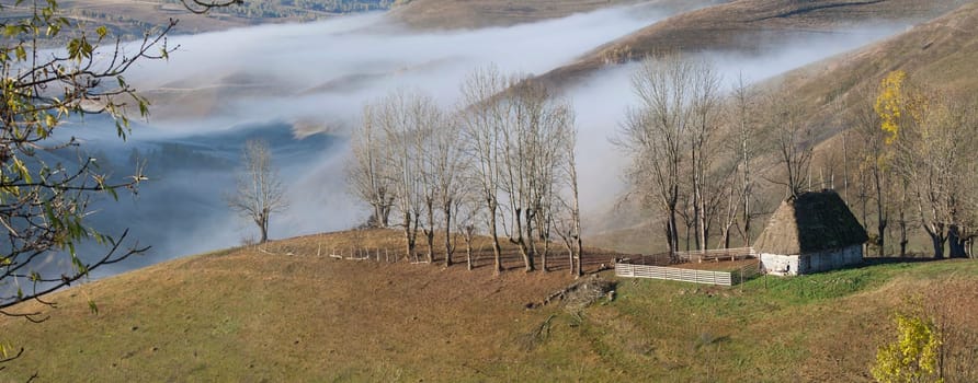 Panoramic view of  Small cottage in the mountains in a foggy autumn morning