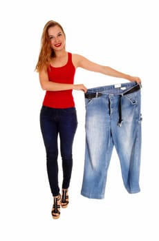 A young slim woman in jeans holding her old big jeans after she lost.much weight, isolated for white background..