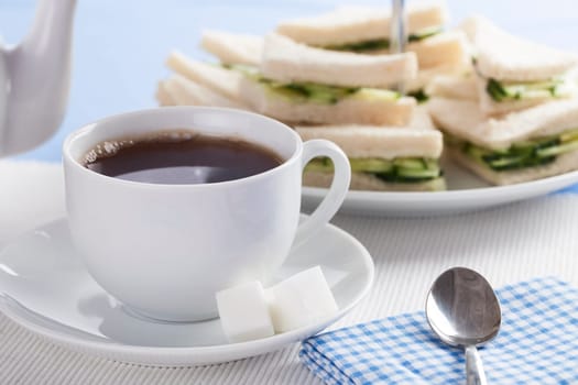 Cup of tea with cucumber sandwiches in background