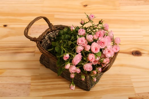 Bunch of small pink Roses in a basket over a wooden table..