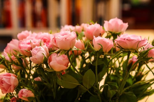 Bunch of small pink Roses in a glass vase over a wooden table..