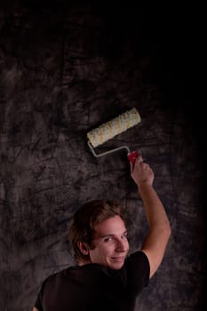 young man painting a black wall with a paint roller