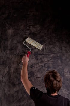 young man painting a black wall with a paint roller