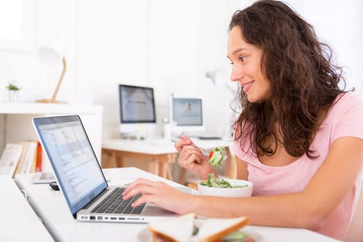 View of a Young attractive student eating salad while working