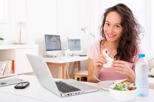 View of a Young attractive student  eating sandwich while working