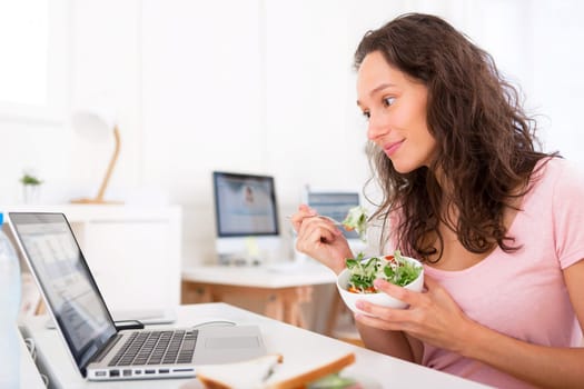 View of a Young attractive student eating salad while working