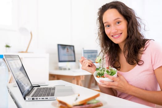 View of a Young attractive student eating salad while working