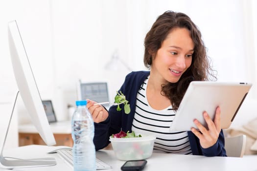 View of a Young attractive student eating salad while using tablet