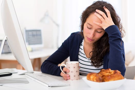 View of a Young tired student taking breakfast while working