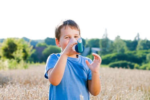 Boy using inhaler for asthma in village with summer sunset
