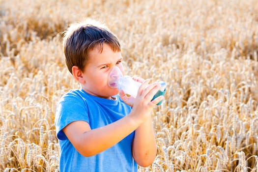 Boy using inhaler for asthma in village with summer sunset