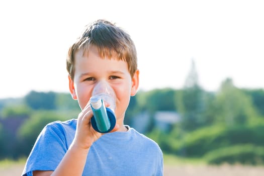 Boy using inhaler for asthma in village with summer sunset
