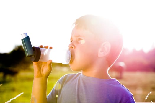 Boy using inhaler for asthma in village with summer sunset