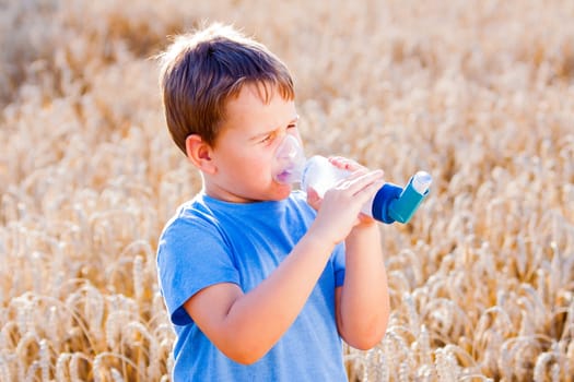 Boy using inhaler for asthma in village with summer sunset