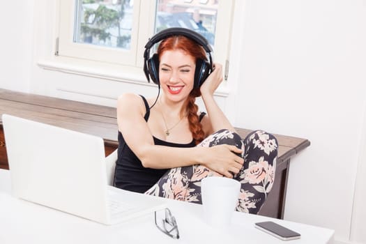 Young woman listens to music on computer with long red hair in living room