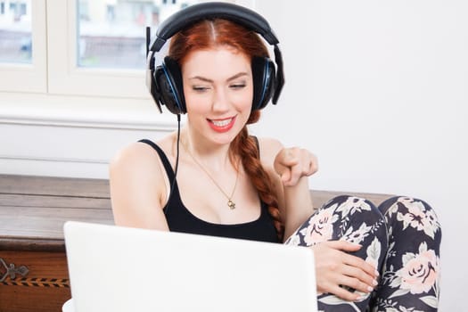 Young woman listens to music on computer with long red hair in living room
