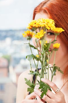 Thoughtful young woman looks out the window in summer with flowers in her hand