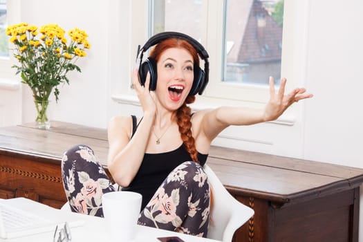 Young woman listens to music on computer with long red hair in living room