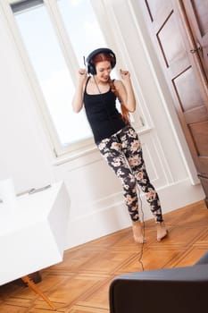 Happy young woman with headphones listens to music in the living room
