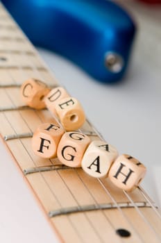 slanted detail view of the fretboard of an electric guitar with letter-wood cubes of the scale lying on the strings low depth of field