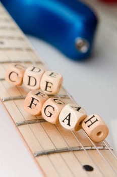 slanted detail view of the fretboard of an electric guitar with letter-wood cubes of the scale lying on the strings low depth of field