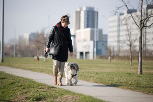 Full-body view of a woman with a mixed-breed dog on a concrete path running towards the camera
