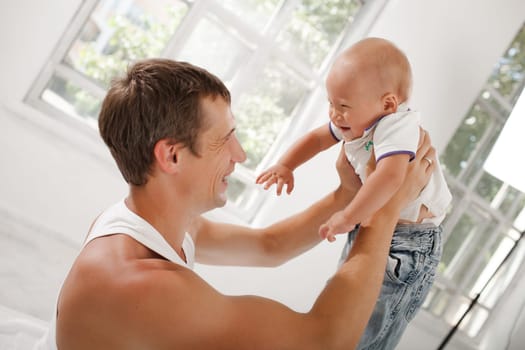 Young smiling father playing with his nine months old son at home on white home background