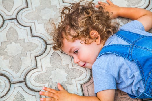 Portrait of 1 year old baby boy laying on the pathway at home, listening to the earth.