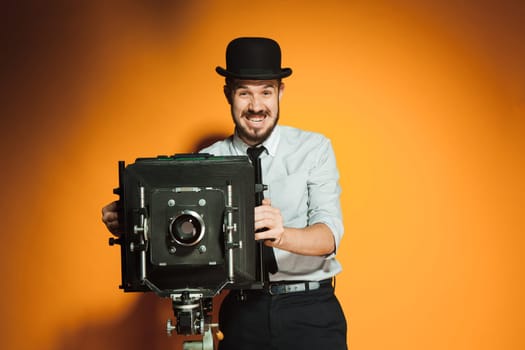 Young smiling man in hat as photographer with retro camera on an orange background