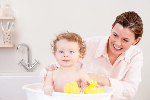 Little girl smiling at the camera whilst being bathed by her mother