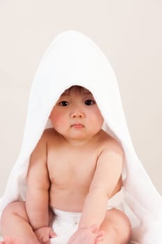 Cute Asian baby sitting with a towel over his head. He is wearing a nappy and is looking at the camera.