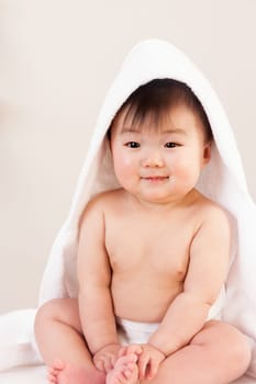 Cute Asian baby sitting with a towel over his head. He is wearing a nappy and is smiling at the camera.