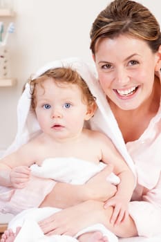 Young mother smiling at the camera whilst drying her baby daughter after a bath