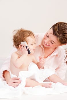 Little girl playing with her mother's phone whilst she gets dried after a bath