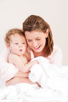Mother playing with her baby daughter after a bath. There is a towel infront of them which the baby girl is holding.