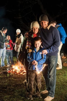 Little boy playing with a sparkler with his parents watching him