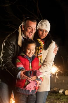 young girl playing with a sparkler with her parents watching her