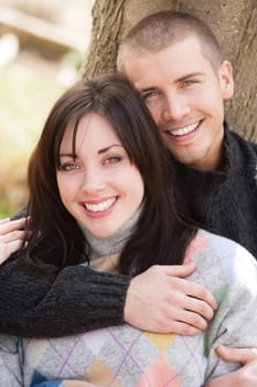 Attractive young couple cuddling out doors. They are both looking at the camera