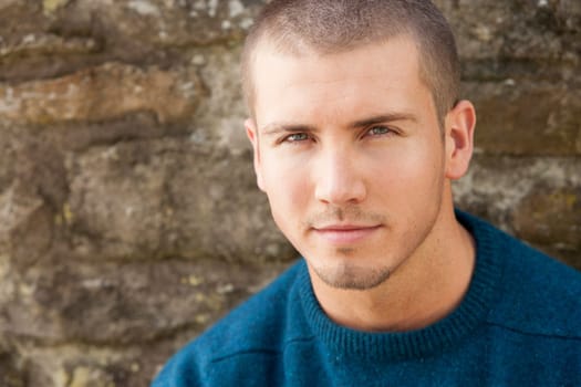 Attractive young man sitting outside. He is looking pensively at the camera.