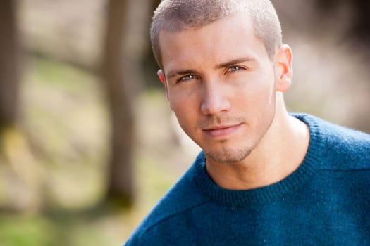 Attractive young man sitting outside. He is looking pensively at the camera.