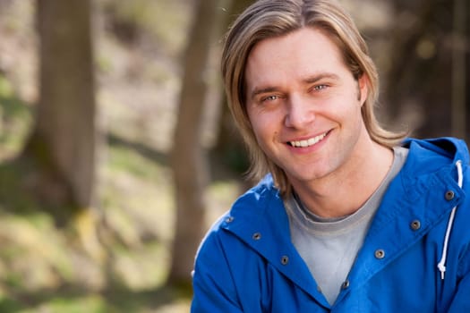 Attractive young man sitting outside. He is smiling at the camera.