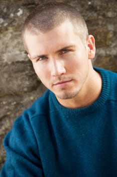 Attractive young man sitting outside. He is looking pensively at the camera.