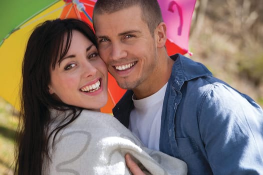 Attractive young couple cuddling out doors. They are both looking at the camera